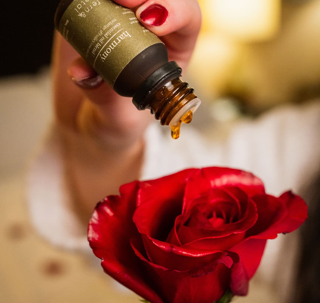 A bottle of harmony dripping oil onto a rose flower.